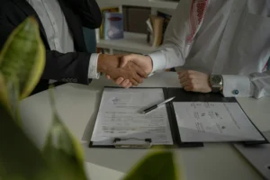 Duas pessoas a apertar a mão sobre um contrato assinado em cima da mesa.