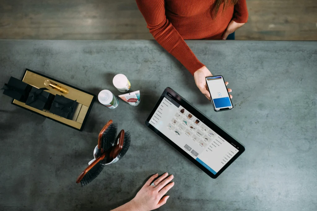 Pessoa a utilizar um telemóvel para pagamento digital junto a um tablet num balcão.