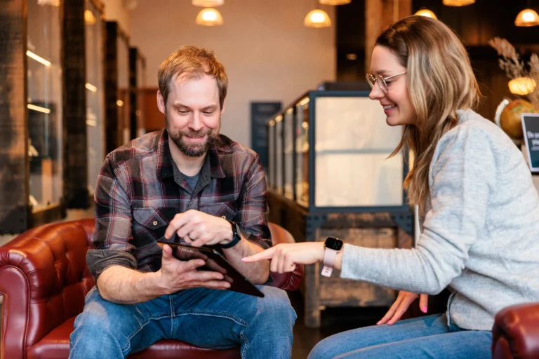 Homem e mulher sentados a analisar um tablet num ambiente de trabalho informal.